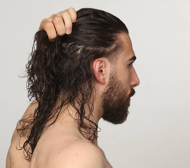 Привлекательная мужская модель с длинными волосами и бородой позирует в студии на изолированном фоне. Стиль, тенденции, концепция моды. - Фото, изображение