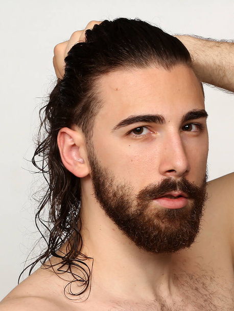 Приваблива чоловіча модель з довгим волоссям і бородою позує в студії на ізольованому фоні. Стиль, тенденції, концепція моди
. - Фото, зображення