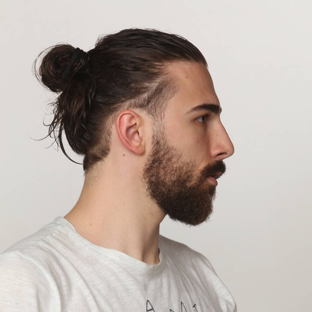 Atrakcyjny model męski z długimi włosami i brodą pozujący w studio na odosobnionym tle. Styl, trendy, koncepcja mody. - Zdjęcie, obraz