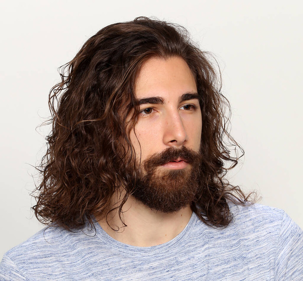 Atrakcyjny model męski z długimi włosami i brodą pozujący w studio na odosobnionym tle. Styl, trendy, koncepcja mody. - Zdjęcie, obraz