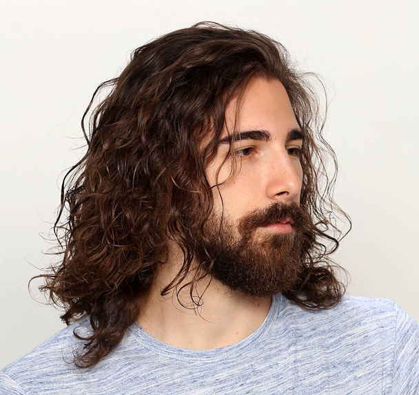 Vonzó férfi modell hosszú hajjal és szakállal pózol a stúdióban, elszigetelt háttérrel. Stílus, trendek, divat koncepció. - Fotó, kép