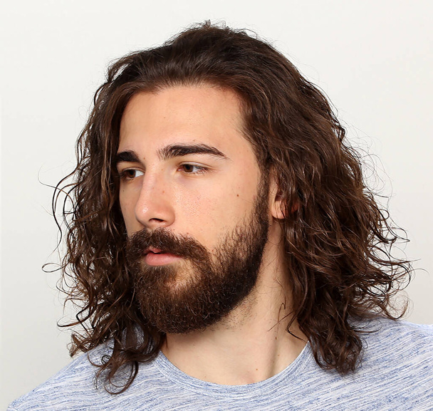 Attractive male model with long hair and beard posing in studio on isolated background. Style, trends, fashion concept. - Фото, изображение