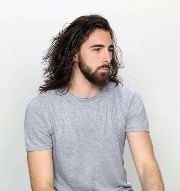 Attractive male model with long hair and beard posing in studio on isolated background. Style, trends, fashion concept. - Photo, image