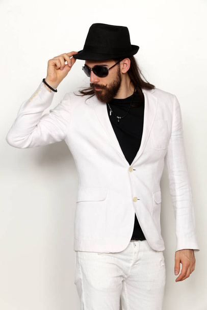 Young, fashionable male model with long hair and beard posing in studio on isolated background. Fashion, business, modeling concept. - Photo, image