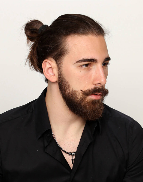 Молода, модна чоловіча модель з довгим волоссям і бородою позує в студії на ізольованому фоні. Мода, бізнес, концепція моделювання
. - Фото, зображення