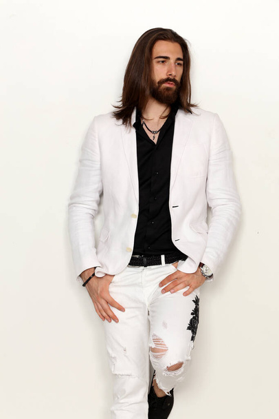 Young, fashionable male model with long hair and beard posing in studio on isolated background. Fashion, business, modeling concept. - Valokuva, kuva