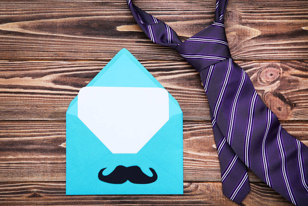 Father's day concept. Envelope with paper mustache and necktie on wooden table - Photo, image