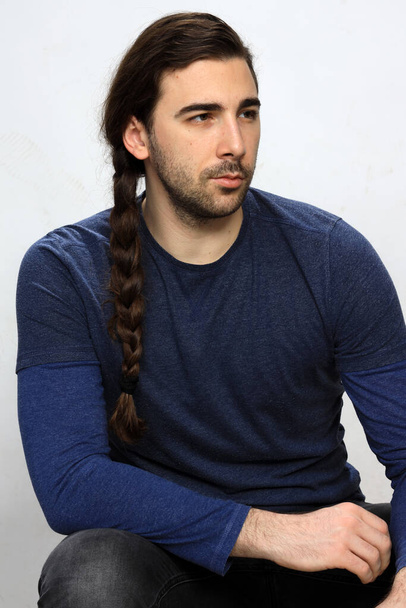 Attractive male model with long hair and beard is posing in studio. Style, trends, fashion concept. - Photo, Image