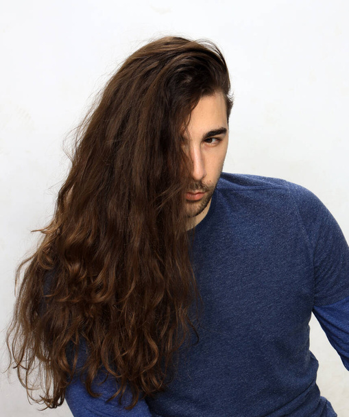 Atractiva modelo masculino con el pelo largo y la barba está posando en el estudio. Estilo, tendencias, concepto de moda. - Foto, Imagen