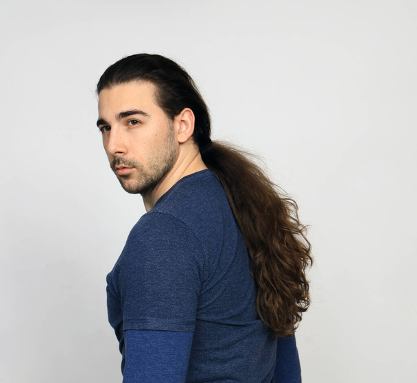 Atractiva modelo masculino con el pelo largo y la barba está posando en el estudio. Estilo, tendencias, concepto de moda. - Foto, imagen