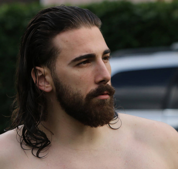 Молодой, привлекательный мужчина-модель с длинными волосами и бородой позирует в природе. Стиль, тенденции, концепция моды. - Фото, изображение