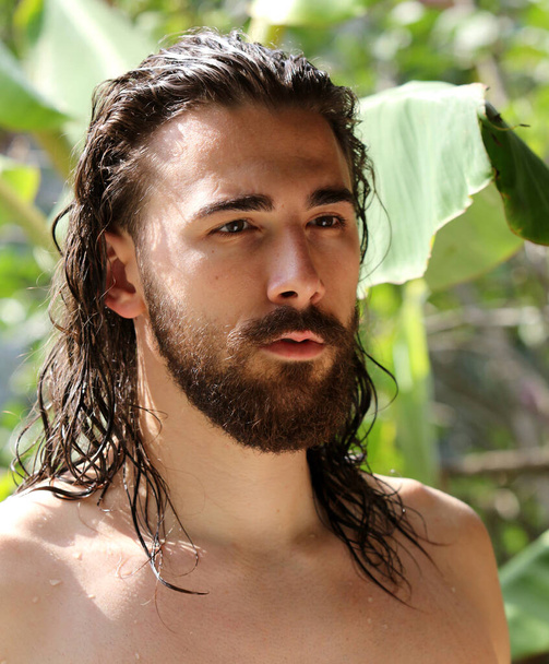 Modelo masculino joven y atractivo con cabello largo y barba posando en la naturaleza. Estilo, tendencias, concepto de moda. - Foto, imagen