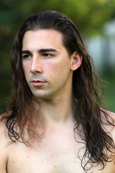 Attractive guy with very long hair is posing in the wild. Modeling and Fashion Concept. - Фото, изображение