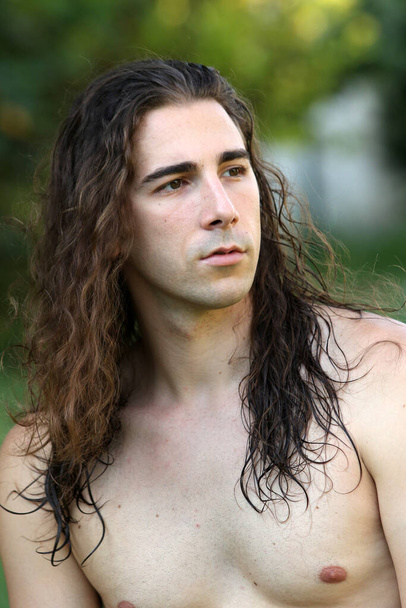 Attractive guy with very long hair is posing in the wild. Modeling and Fashion Concept. - Фото, зображення