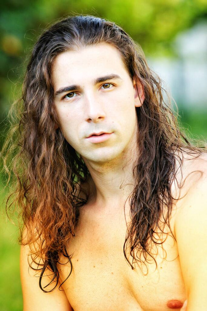 Atraktivní chlap s velmi dlouhými vlasy pózuje v divočině. Koncept modelování a módy. - Fotografie, Obrázek