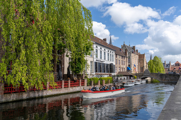 Brugge, België - 12 mei 2021: toeristen genieten van een idyllische boottocht over de grachten in het historische centrum van Brugge - Foto, afbeelding