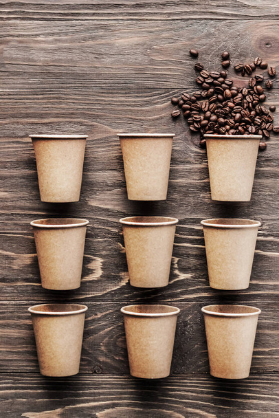 Kahvipaperimukeja ja yksi kuppi kahvipapuja puupohjalla. Kuvio ja luova tausta käsite kahviloita - Valokuva, kuva