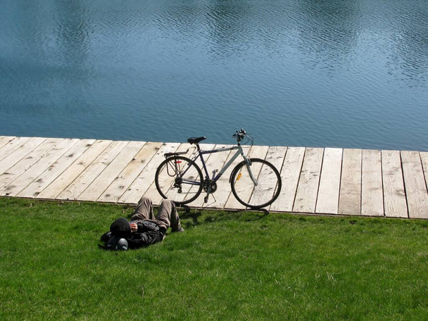 Bicyclette et homme relaxant couché sur l'herbe près de l'étang, Granville Island, Vancouver, BC, Canada - Photo, image
