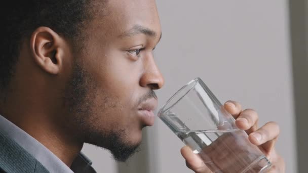 Nyugodt jóképű afro-amerikai srác etnikai férfi kezében üveg ásványi természetes tiszta víz, hogy korty élvezze a frissítő és szomjúság enyhítésére, élvezi a napi egészségügyi rutin, egyedül beltérben. - Felvétel, videó