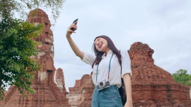 Jonge Aziatische backpacker blogger vrouw casual nemen selfie video gesprek op mobiele telefoon delen live online voor publiek reizen samen op pagode oude stad, Lifestyle toeristische reizen concept. - Video