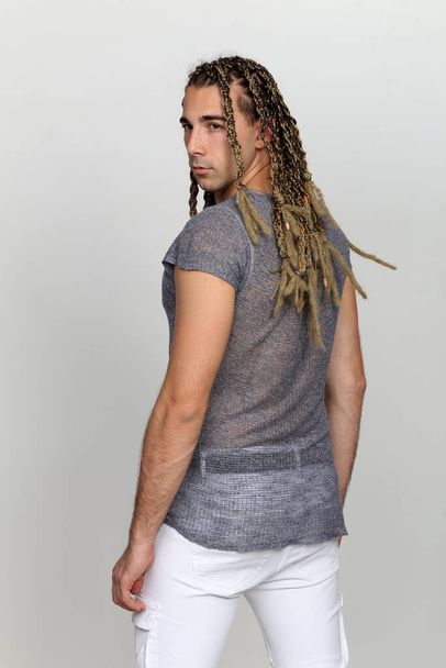 Atraktivní blonďatý mužský model s kombinací copů a dredů pózující ve studiu na izolovaném pozadí. Styl, trendy, módní koncept. - Fotografie, Obrázek