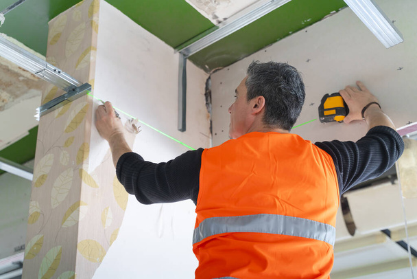 in het werken met op een ladder op de bouwplaats binnenshuis bouwvakker meten steunbalk - Foto, afbeelding