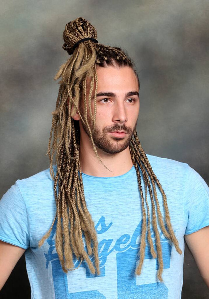 Attractive blonde male model with combination of braids and dreadlocks posing in studio on isolated background. Style, trends, fashion concept. - Photo, Image