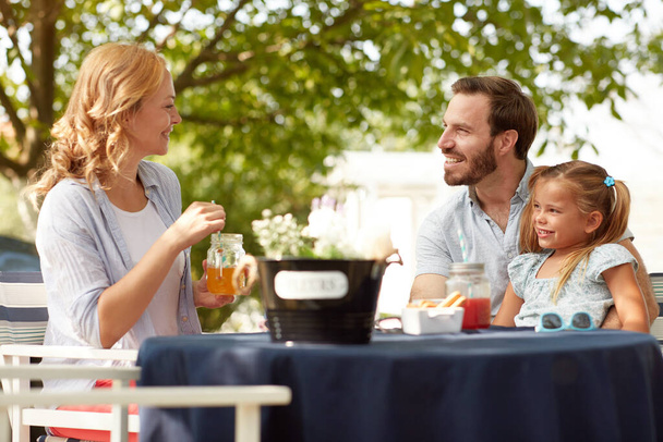 beardy caucasian male with little girl in his lap looking at blonde female, smiling, sitting at outdoor table - Photo, Image