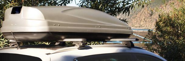 Auto kofferbak op het dak. 4WD auto met koffer op het dak bevestiging aan het rek systeem. Close-up uitzicht van de auto Roof Box op het dak. Reizen en reizen Auto Toerisme Landschap met Mountain and Sea Beach. - Foto, afbeelding