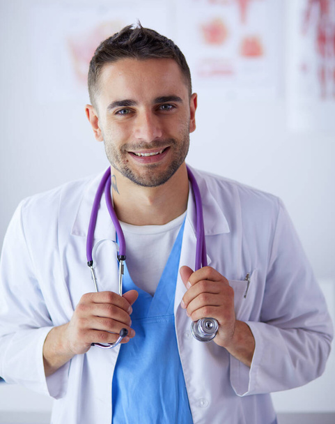 Young and confident male doctor portrait standing in medical office. - Fotoğraf, Görsel