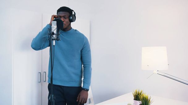 Egy férfi, aki fejhallgatót hord, és egy dalt énekel egy mikrofonba egy stúdióban. - Fotó, kép