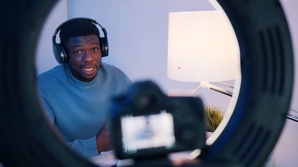 Nahaufnahme des Kamerasystems, auf dem ein afroamerikanischer Mann mit Kopfhörern am Tisch sitzt und etwas erklärt. Konzept von Online-Kursen oder Podcasts.  - Foto, Bild