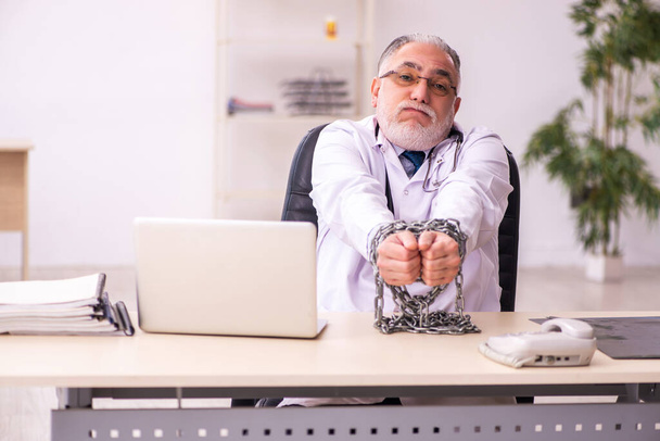 Αλυσοδεμένος ηλικιωμένος άνδρας γιατρός που εργάζεται στην κλινική - Φωτογραφία, εικόνα