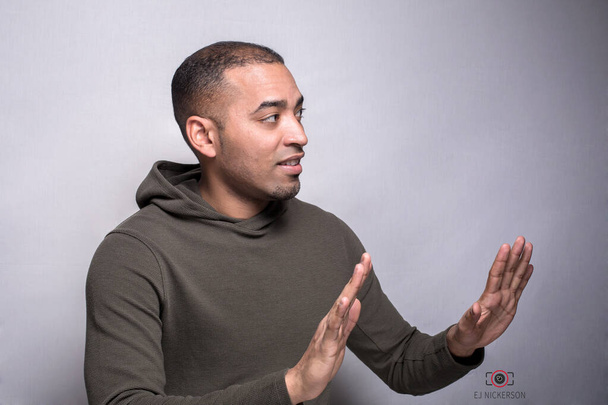A portrait of a Hispanic, Latino Black man in green hoodie gesturing a rejection sign with his hands, isolated on grey - Foto, Bild