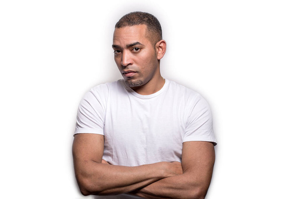 A portrait of a Latino Hispanic black man with crossed hands, looking with no trust in the camera, isolated on grey - Zdjęcie, obraz