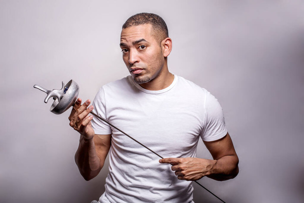 Portrait d'un athlète hispanique d'âge moyen portant un t-shirt blanc, avec la flèche d'épée dans les mains, isolé sur le fond gris - Photo, image