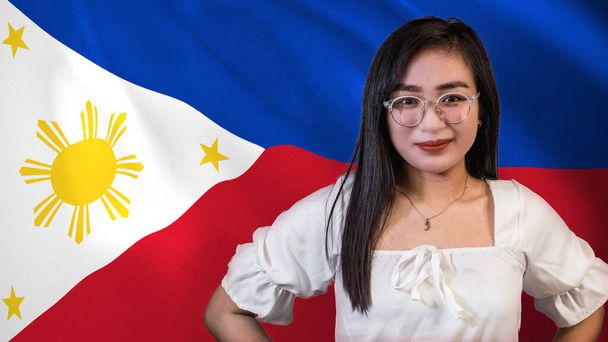 A proud and patriotic young Filipina woman, in front of a waving Philippine flag. - Photo, Image