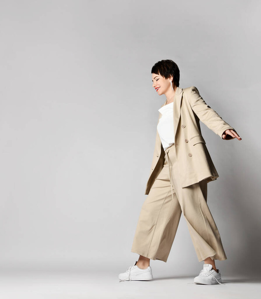 Joyful adult pretty woman walks in beige business smart casual pantsuit and sneakers. Stylish business female wear - Foto, Imagem