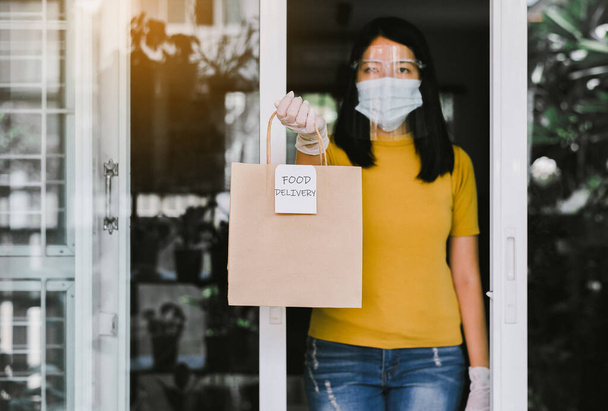 Woman holding takeaway food in paper bag from delivery service during coronavirus pandemic situation at home - Photo, image