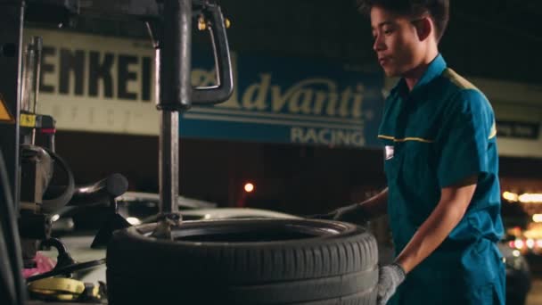 Professional car mechanic changing a car tire on lifted automobile at repair service station. Wheel alignment work at workshop night. Skillful Asian guy in uniform fixing car. Car service repair. - Footage, Video