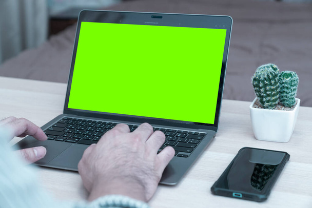 Nuori liikemies työskentelee kannettavan tietokoneen kotona, takana näkymä vihreä ruutu liikemies kädet kiireinen käyttää kannettavaa toimistossa työpöytä, kirjoittamalla tietokoneen istuu puinen pöytä - Valokuva, kuva