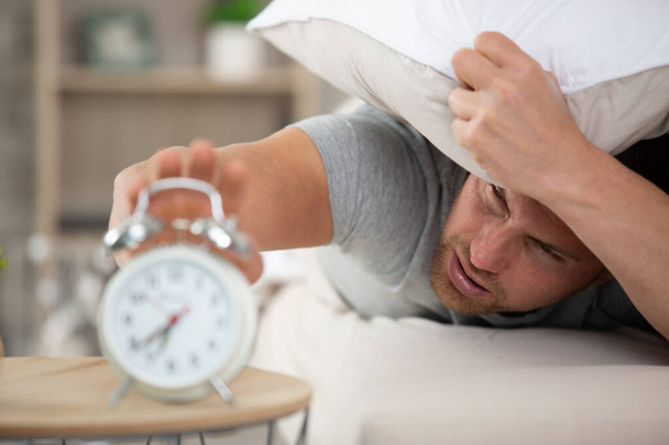 annoyed man laying in bed with alarm clock ringing - Фото, зображення