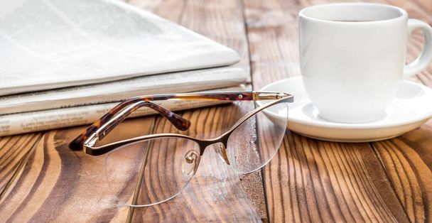 Eyeglasses with newspapers and cup of coffee on the table. - Photo, Image