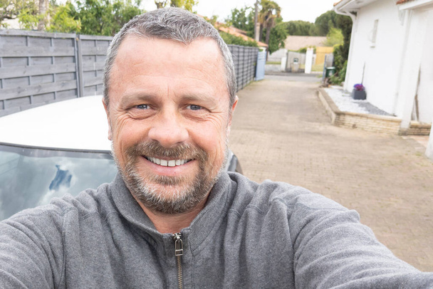 man van middelbare leeftijd knap maken selfie in huis steegje tuin guy blij met smartphone - Foto, afbeelding