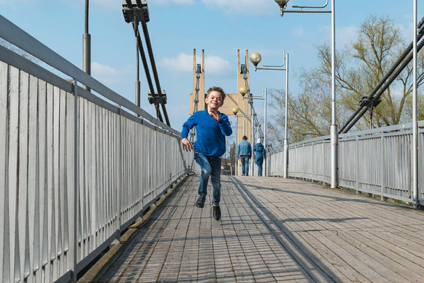 A little boy walks in the park near a suspension bridge with metal ropes - Foto, imagen