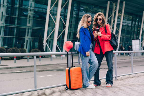 Deux filles heureuses utilisant le vol d'enregistrement smartphone ou l'enregistrement en ligne à l'aéroport ensemble, avec des bagages. Voyages aériens, vacances d'été - Photo, image