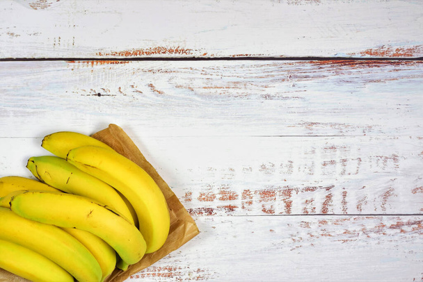 Group of bananas on a paper bag and white rustic table. Copy space. - Foto, Imagem
