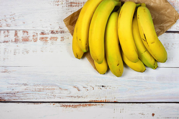 Group of bananas on a paper bag and white rustic table. Copy space. - Foto, immagini