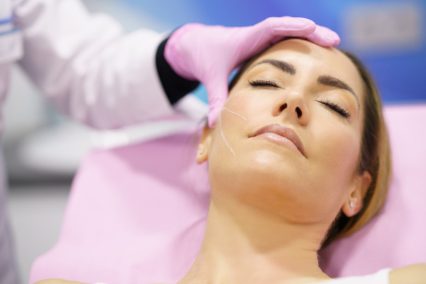 Médico pintando el área de una cara de mujer donde se inyectarán los hilos de tratamiento de sutura PDO. - Foto, imagen