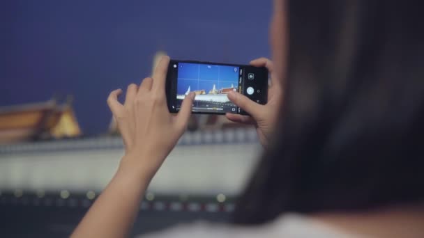 Feliz joven turista de Asia chica con estilo casual mantenga el teléfono móvil relajarse alegre tomar foto pacífica del templo en Bangkok por la noche. Estilo de vida turista viaje vacaciones concepto. - Imágenes, Vídeo